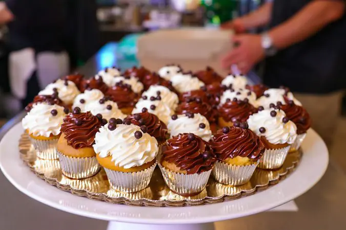 A plate of cupcakes with chocolate and vanilla frosting, topped with small chocolate spheres, displayed on a table.