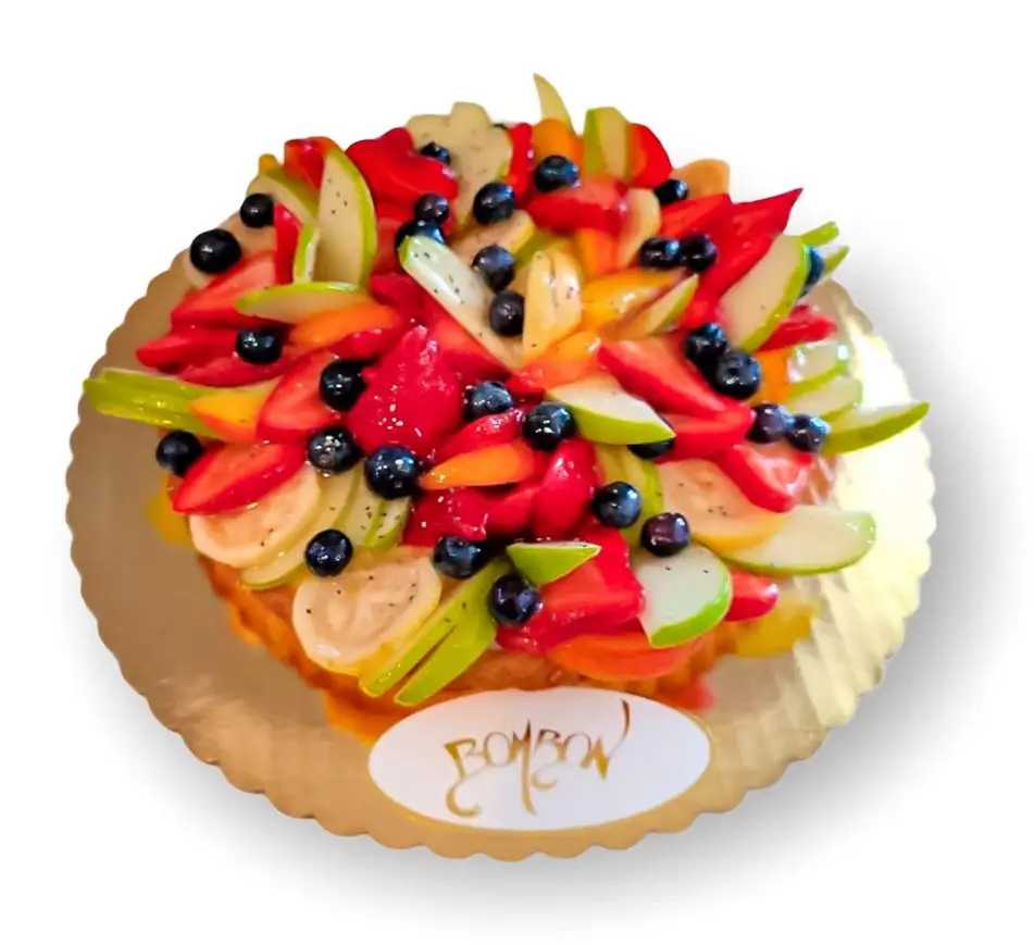Fruit tart with blueberries, strawberries, kiwi, bananas, and apple slices on a gold base labeled "Bombon.
